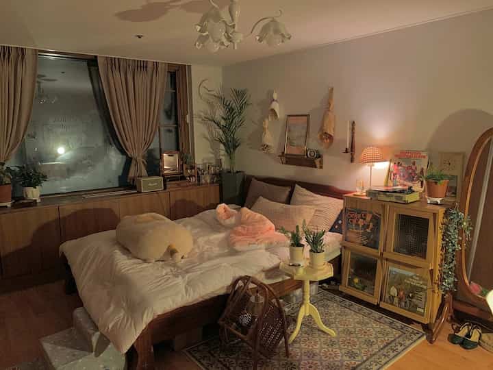 Bedroom with wood tones and pinkish lighting, featuring wooden cabinet and cozy bedding creating a vintage atmosphere