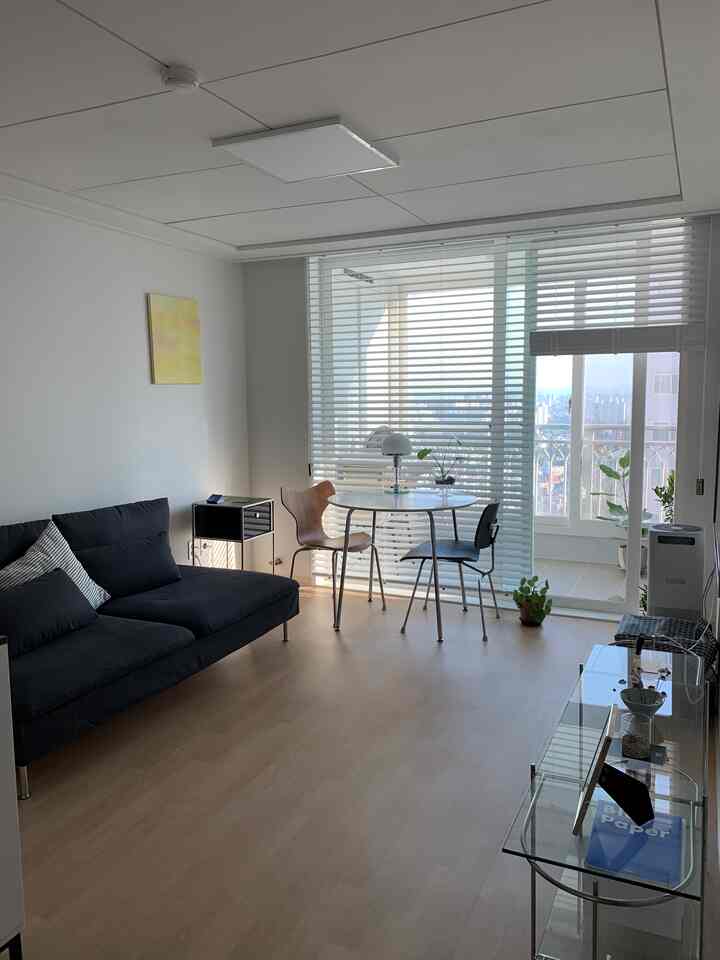 白とナチュラルトーンのリビング、黒いソファと丸いダイニングテーブルが配置されたモダンな空間