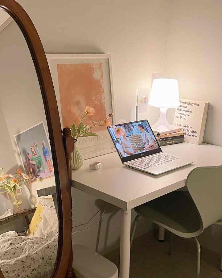 白とナチュラルトーンの小さな部屋、白いデスクと椅子、全身鏡、暖かい照明とポスターが配された雰囲気のあるインテリア