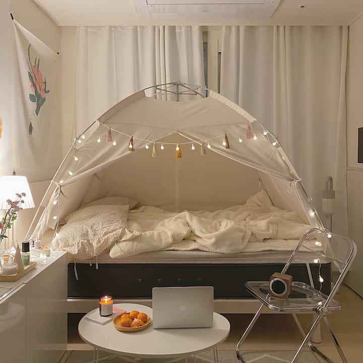 White and natural toned bedroom featuring a bed with heating tent and blackout curtains, creating a cozy winter atmosphere