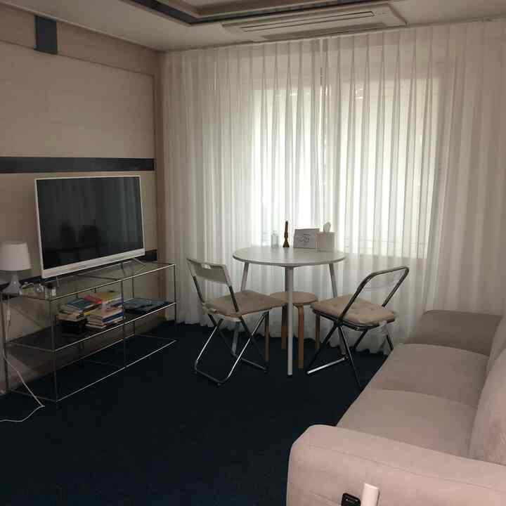 A cozy living room in white and gray tones featuring a beige sofa, TV stand, and a small round dining set
