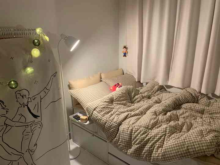 Beige and white toned bedroom featuring a bed with checkered duvet and pillows, blackout curtains, and a floor lamp creating a cozy atmosphere