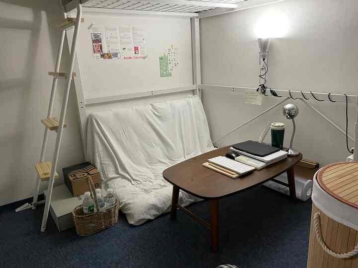 ホワイトトーンの狭いロフト空間、ソファベッドとダークウッドの机が配置された実用的で居心地の良いホームオフィス