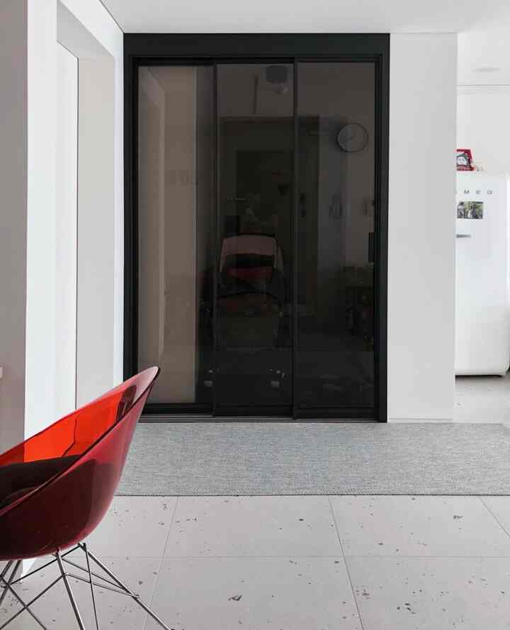 Modern entrance space with white walls and gray carpet, featuring a closed transparent middle door with black framing