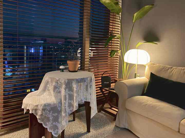 Wood tone and white living room featuring a round table with tablecloth, sofa, green plant, and warm lighting creating a cozy atmosphere