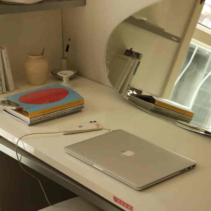 White-toned compact home office space featuring a desk with laptop and mirror, presenting a simple and clean interior