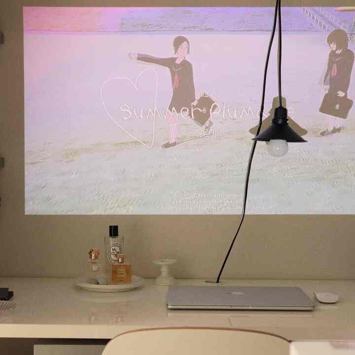 白を基調としたホームオフィス空間、シンプルなデスクにペンダントライトとノートパソコン、香水の小物が配置された清潔感のあるインテリア