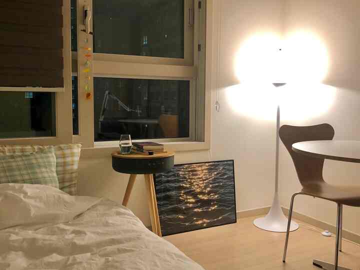 ホワイトと木目調が調和する小さな一人暮らしの寝室、フロアランプと丸いサイドテーブルが配置された暖かい空間