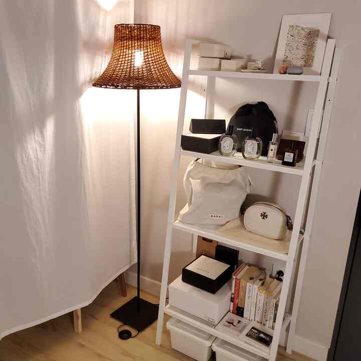 ホワイトとウッドトーンのウォークインクローゼット、棚とラタンシェードのフロアランプが配置された落ち着いた印象的な空間