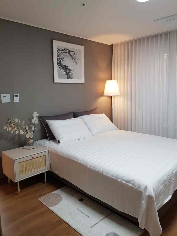 A bedroom featuring white and natural tones with hotel-like style bedding and furnishings, creating a clean and cozy atmosphere