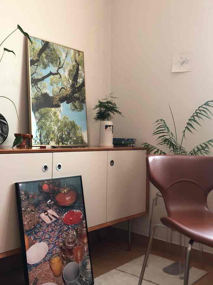 ベージュの壁とサイドボード、植物と額縁が配置された居心地の良いリビングの隅の空間