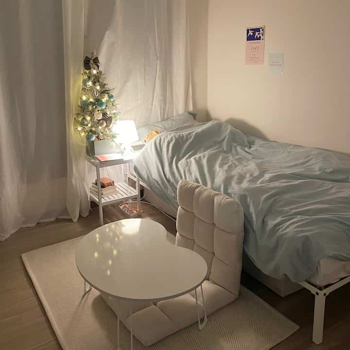 Warm beige-toned studio bedroom featuring a beige rug, low floor table, and cozy Christmas tree decor