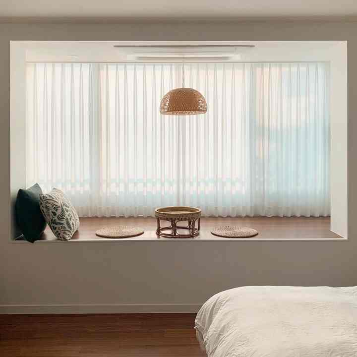 Natural-toned white and brown bedroom featuring rattan pendant light and rattan seating table by the window with cushions