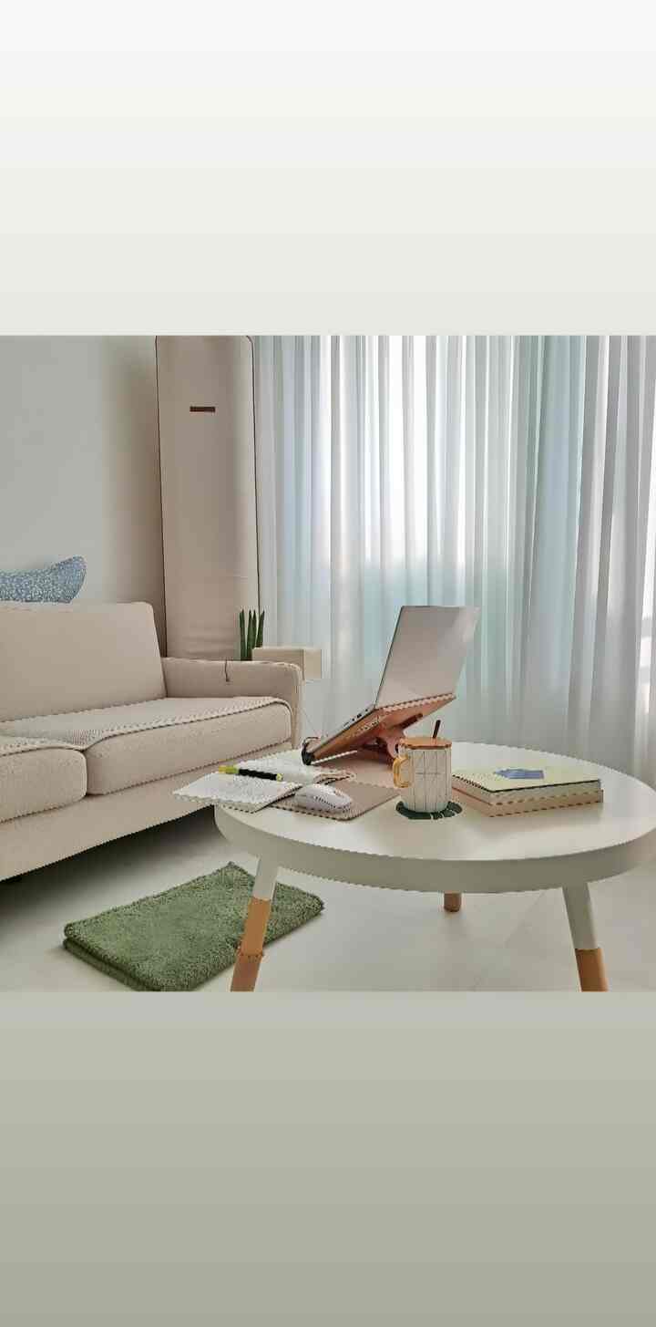 ベージュとホワイトの色調のリビング、ベージュのソファと白い円形テーブルにノートパソコンと本が置かれた印象的なモダンな空間