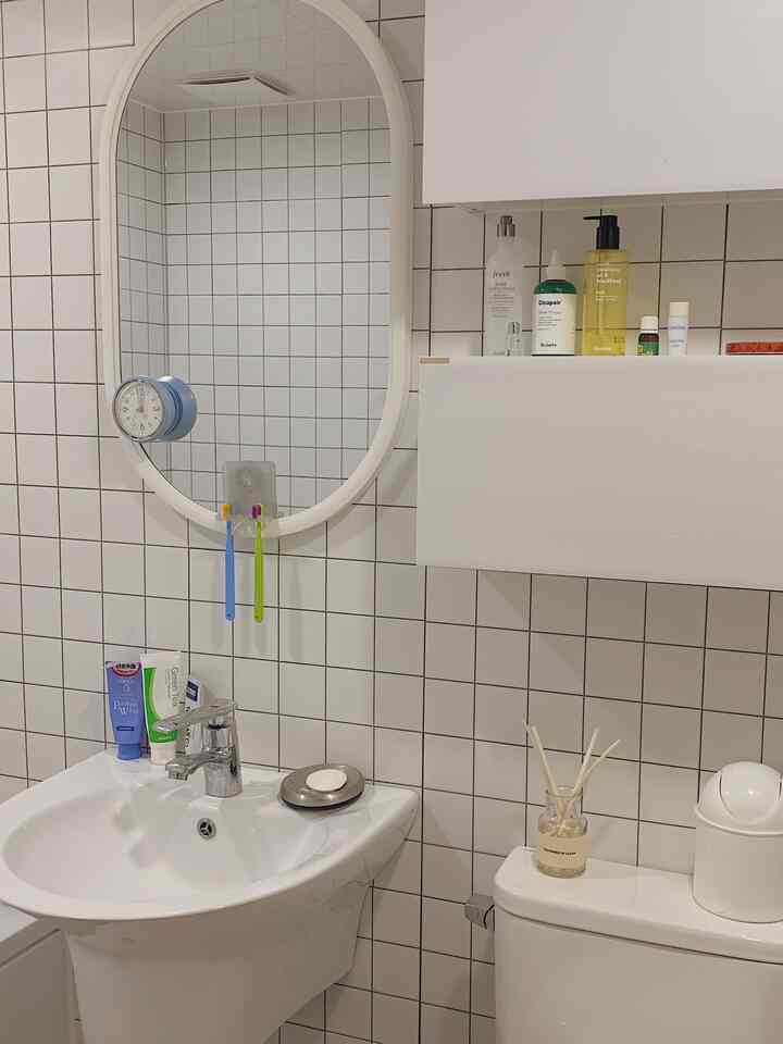 Clean bathroom space with white tiled walls, oval mirror, and diffuser on toilet tank