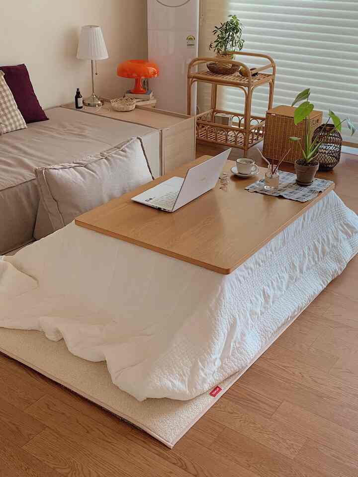 ナチュラルな色調のリビング、こたつテーブルとベージュのソファ、ラタン家具が配置された温かみのあるインテリア