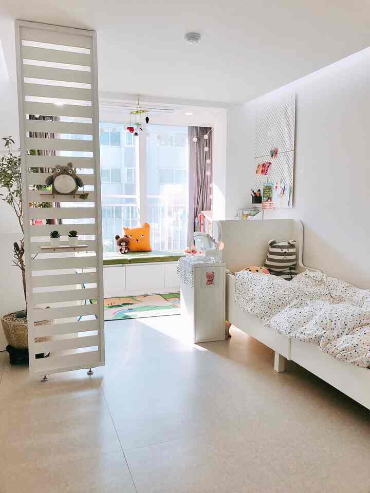 Bright white and natural-toned kids' bedroom featuring a room divider, child's bed, desk, creating a bright and cozy atmosphere
