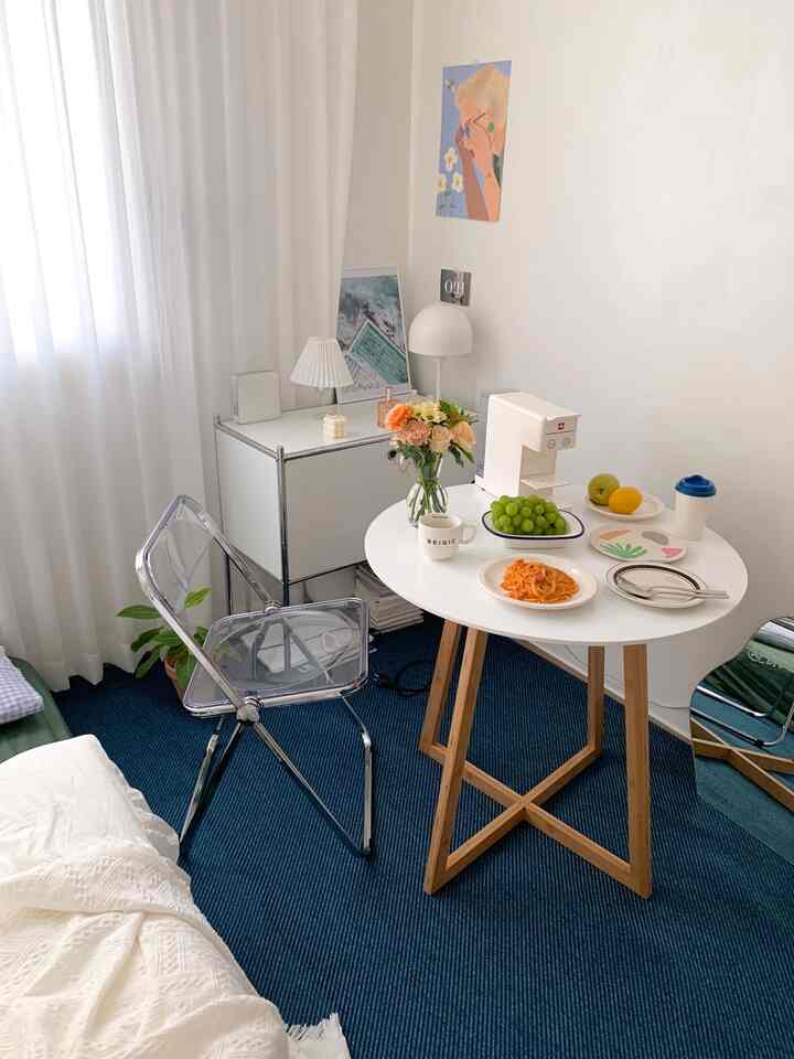 白と青のトーンが印象的な小さな空間、透明な椅子と丸いダイニングテーブルにコーヒーマシンと花瓶が配置されたモダンなホームカフェインテリア