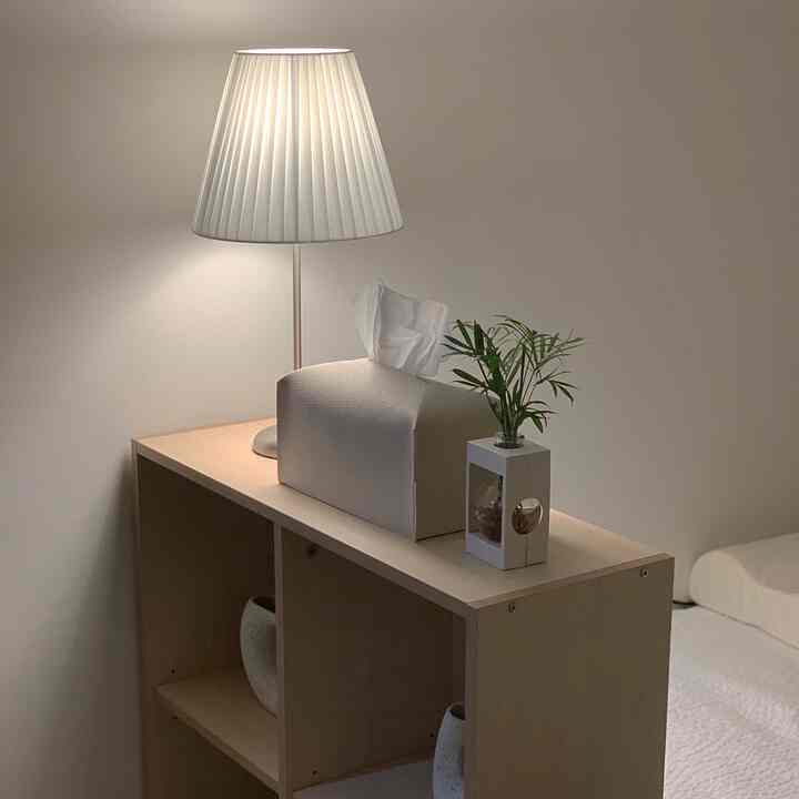 白とベージュのトーンの寝室、木製収納棚の上にテーブルランプと観葉植物が置かれたシンプルな空間