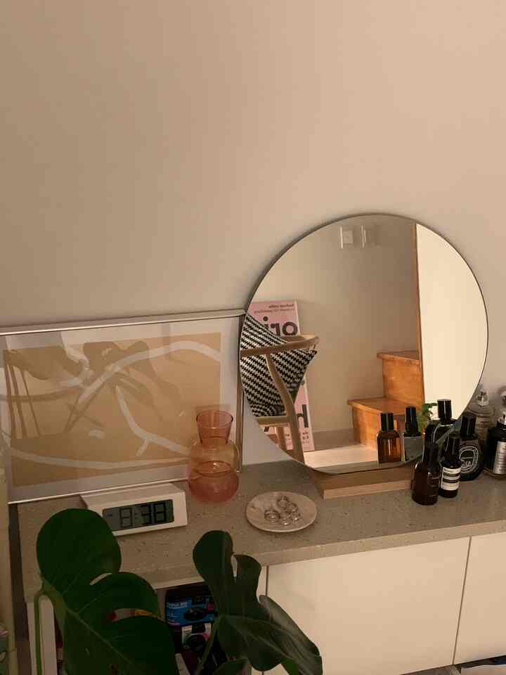 Beige-toned wall with a round mirror, poster, and digital clock in a natural-style studio apartment interior
