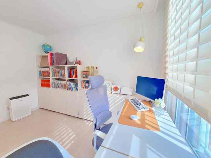 A small study with white walls and wood-tone flooring, featuring a desk, office chair, and bookshelf arranged neatly