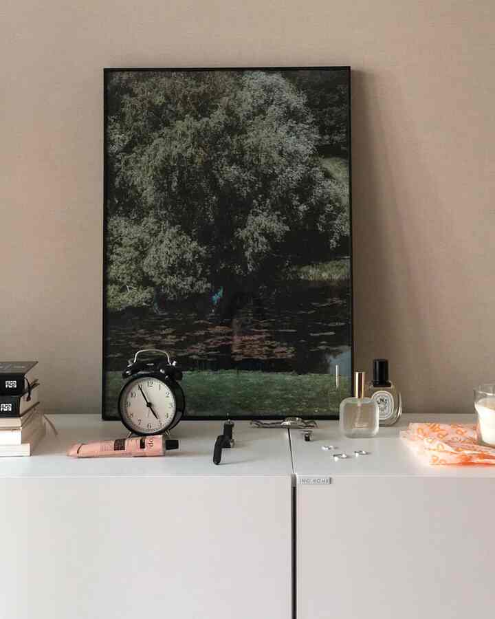 柔らかなナチュラルカラーの書斎空間、ホワイトのチェストの上に時計とポスターが配置された清潔感のあるインテリア