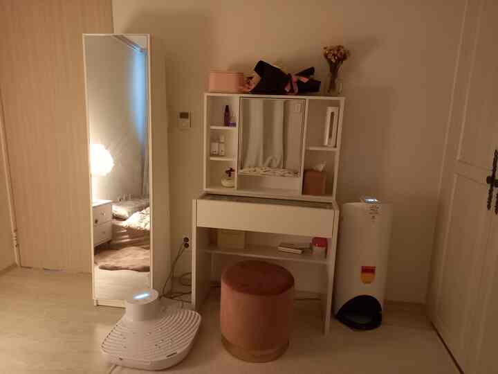 白とピンクの色調の寝室の化粧台スペース、スツールとペット用自動給餌器が配置された雰囲気のあるインテリア