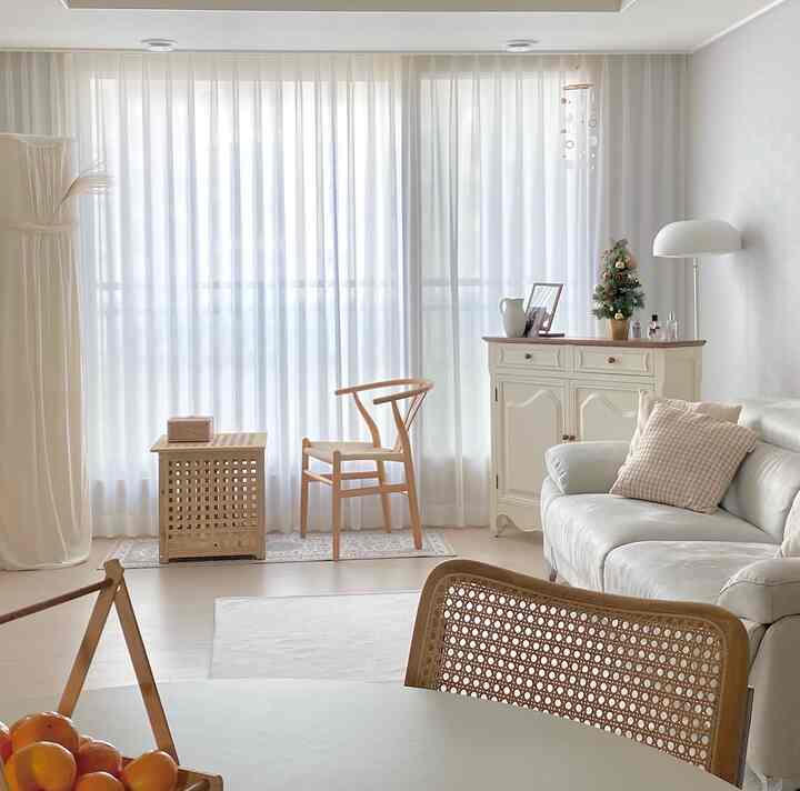 A white and natural-tone living room featuring a rattan chair and Christmas tree creating a cozy atmosphere