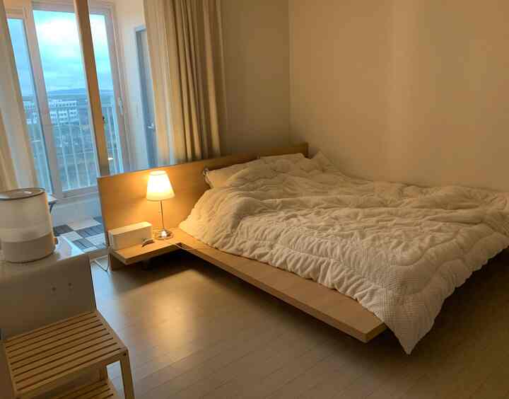 暖かみのある木目調の床とベッドが配置された落ち着いた二人用寝室、明るい照明とカーテンが快適な雰囲気を演出。