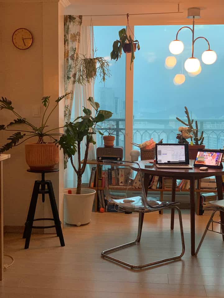 Warm wood tone living room and home office featuring plants and a round table with city view through large window