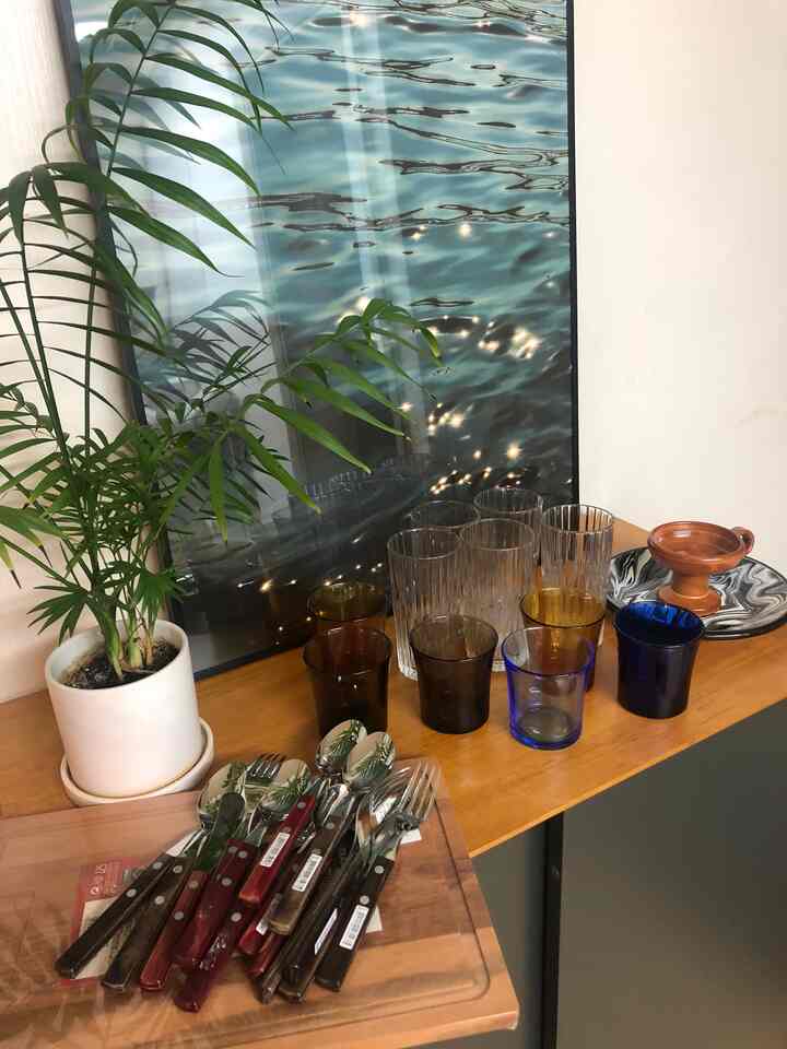 Cozy indoor space with natural wood tone table topped with colorful glassware and cutlery against a water-themed poster background