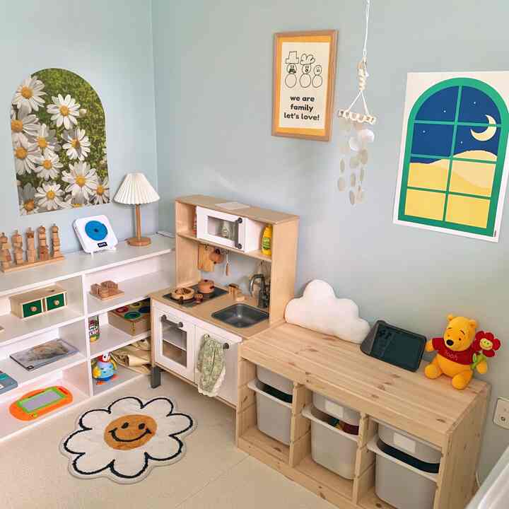Light blue-walled kids' room featuring natural wood furniture with a play kitchen set and toy storage creating a baby-friendly atmosphere