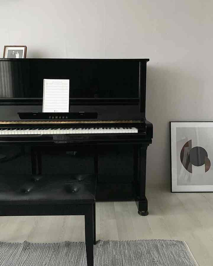 Charcoal-toned bedroom featuring a central black upright Yamaha piano with matching bench, and an abstract poster frame resting on the right floor, creating a minimalistic ambiance