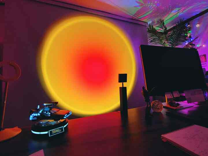 黄色と赤のムード照明が特徴のゲームルーム兼ホームオフィスのデスクスペース、ミニマルな小物とLEDライトが配置された落ち着いた雰囲気のインテリア