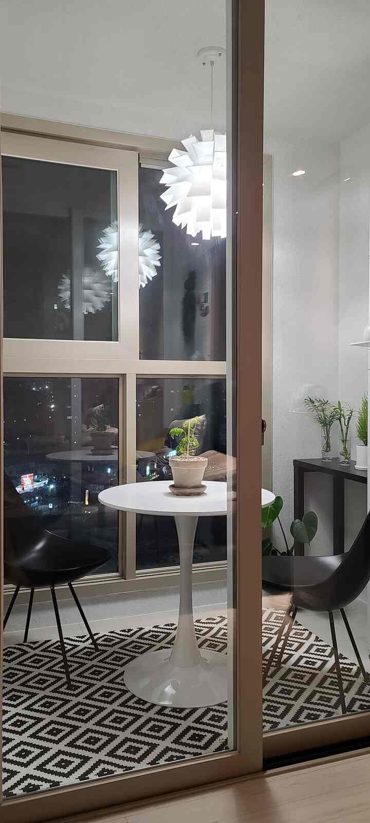 白と黒のトーンのバルコニー空間、丸テーブルと椅子、ペンダントライトが配置されたモダンで落ち着いた雰囲気のインテリア