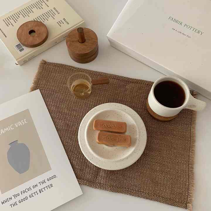 Beige and wood tone home cafe setup featuring coffee cup, cookies on plate, and cozy, natural atmosphere
