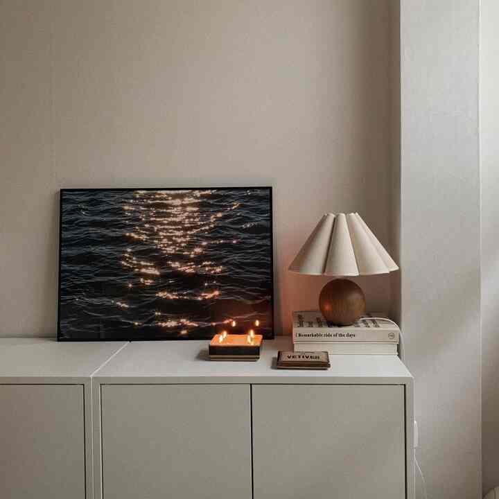 白を基調としたミニマルな空間で、大きな収納キャビネットの上にポスターとテーブルランプが配された落ち着いた雰囲気のインテリア