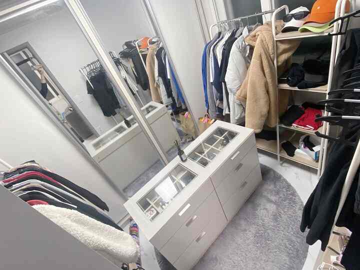 White and gray toned compact walk-in closet featuring a central island drawer chest and a round rug, creating a neat atmosphere