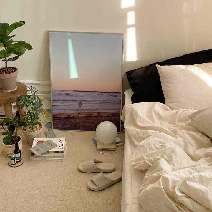 温かみのあるベージュ調の寝室、ベージュの寝具とラグ、サンディエゴの夕日ポスターが配置された雰囲気のあるインテリア