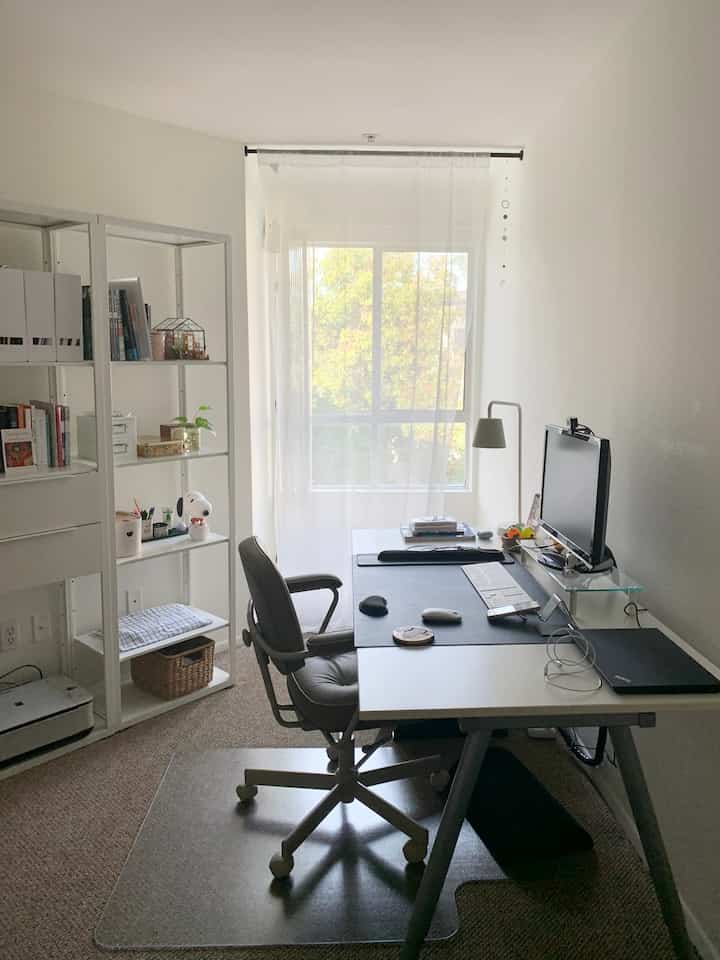 白とナチュラルカラーのホームオフィス、窓際に配置された机とオフィスチェアがある清潔感のある作業空間