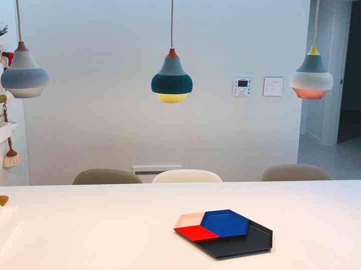 Modern kitchen space with white background and table, featuring colorful round pendant lights and vivid trays on the table