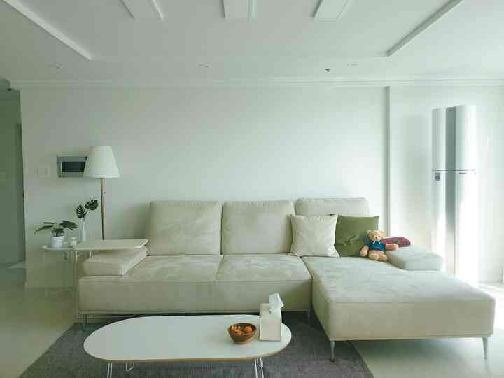 明るいベージュの色調のリビング、中央に大きなコーナーソファとサイドテーブル、フロアランプが配置されたすっきりとした空間