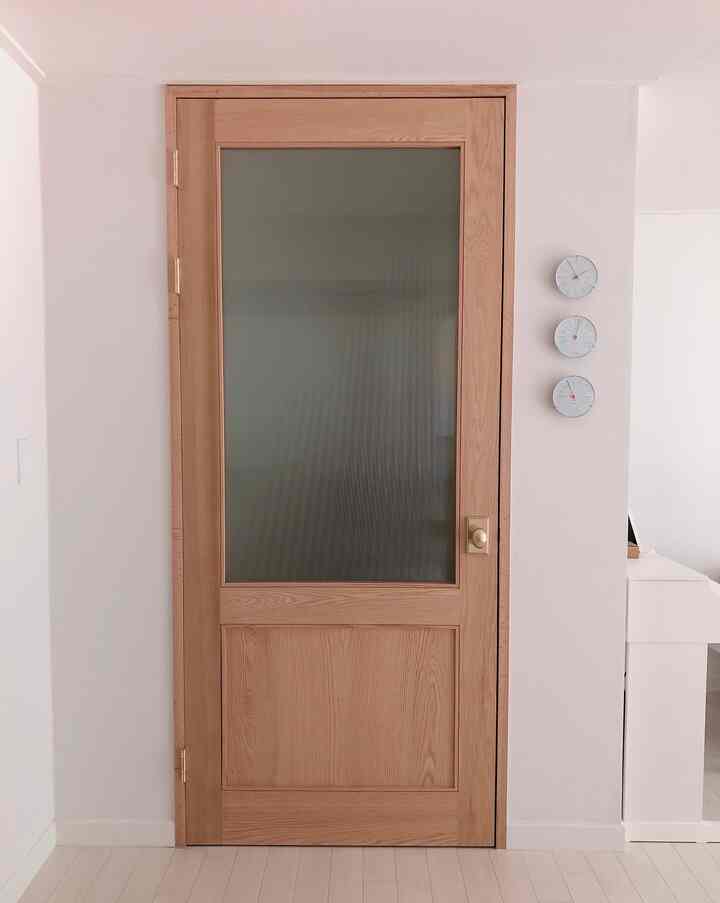 Modern entrance space with white walls and wood tone door, featuring three clocks neatly arranged on the wall with a minimalistic interior