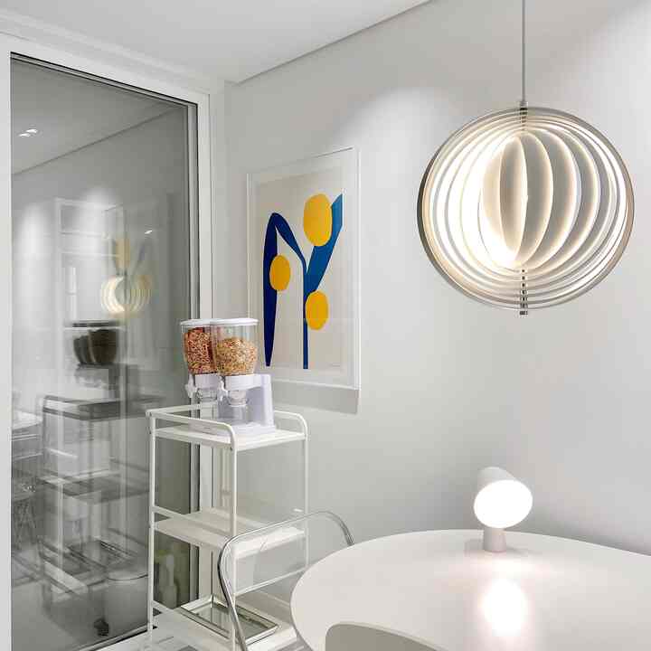 White-walled kitchen with Nordic style kitchen cart, abstract blue and yellow wall art, modern pendant light, and round dining table in a clean space