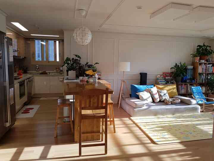 Natural tone wood flooring with wooden dining table, bright sofa and blue armchair in a natural living room and kitchen space