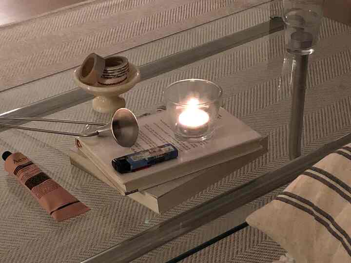 Transparent glass table in living room features a lit candle, hand cream, books, and simple cozy decor