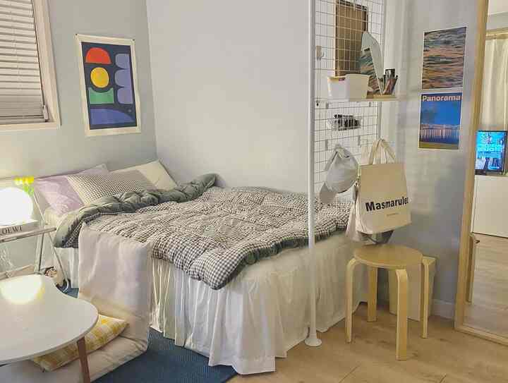 Natural toned bedroom featuring a single bed, stool, blue rug, and posters arranged in a cozy compact space