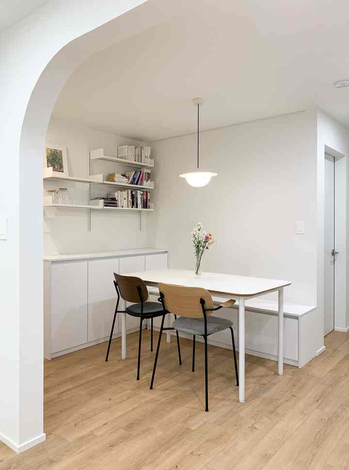 Natural wood and white-toned two-person dining room featuring wall storage cabinets and shelves in a simple cozy setting