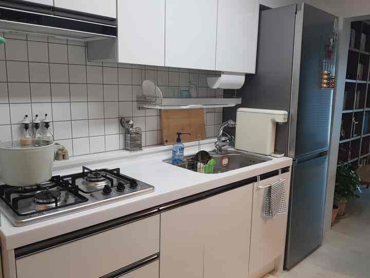Modern kitchen with bright white tiles and countertop, featuring a water purifier and neatly organized cooking utensils
