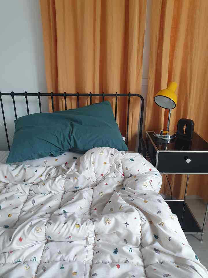 オレンジ色のカーテンと黒いベッドフレームが調和する一人暮らし用モダンな寝室のインテリア